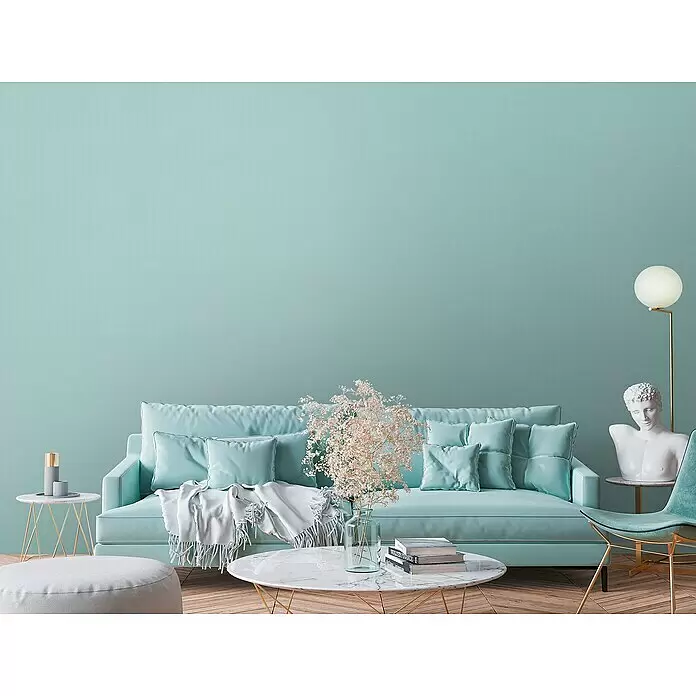 A.S. Création Metropolitan Stories Travel Styles Vliestapete - Minzblau, Uni, 10,05 x 0,53 m - Türkises Sofa mit Kissen und einem weißen Überwurf in modernem Wohnzimmerambiente.