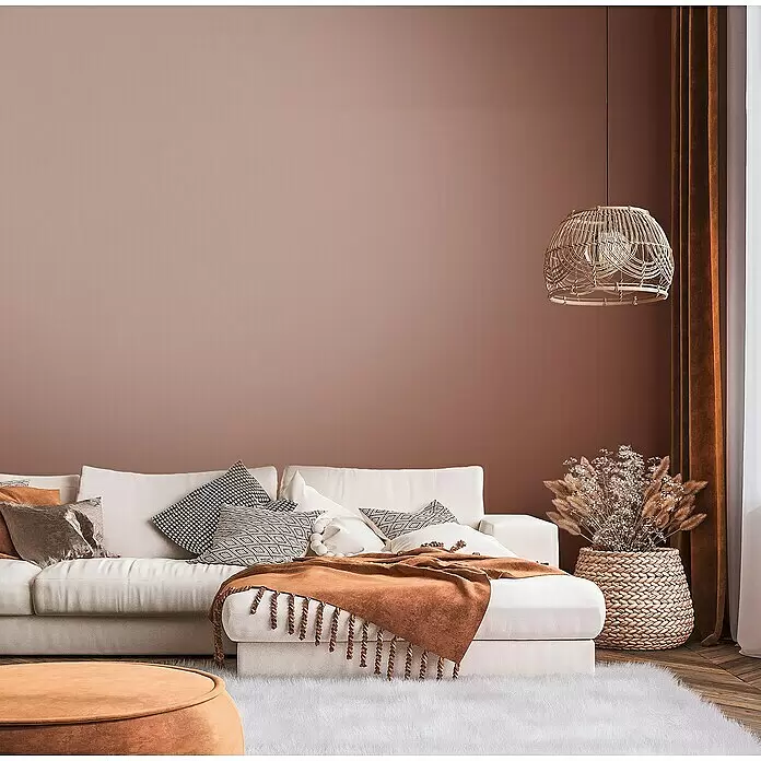 A.S. Création Metropolitan Stories Travel Styles Vliestapete - Rost, Uni, 10,05 x 0,53 m - Ein gemütliches Wohnzimmer mit weißem Sofa, rostfarbenen Akzenten, weichem Teppich und geflochtener Pendelleuchte, in warmer, erdiger Ästhetik.