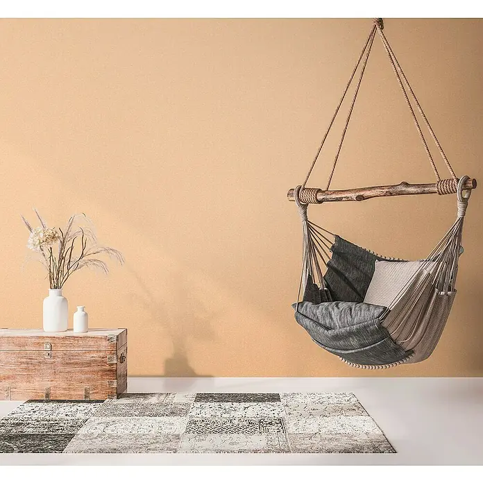 A.S. Création Metropolitan Stories Travel Styles VliestapeteMelange-Orange, Uni, 10,05 x 0,53 m - Eine stilvolle Hängehöhle mit Kissen und Decke, die zum Entspannen einlädt, ergänzt durch einen Teppich und Dekoelemente in einem gemütlichen Raum.