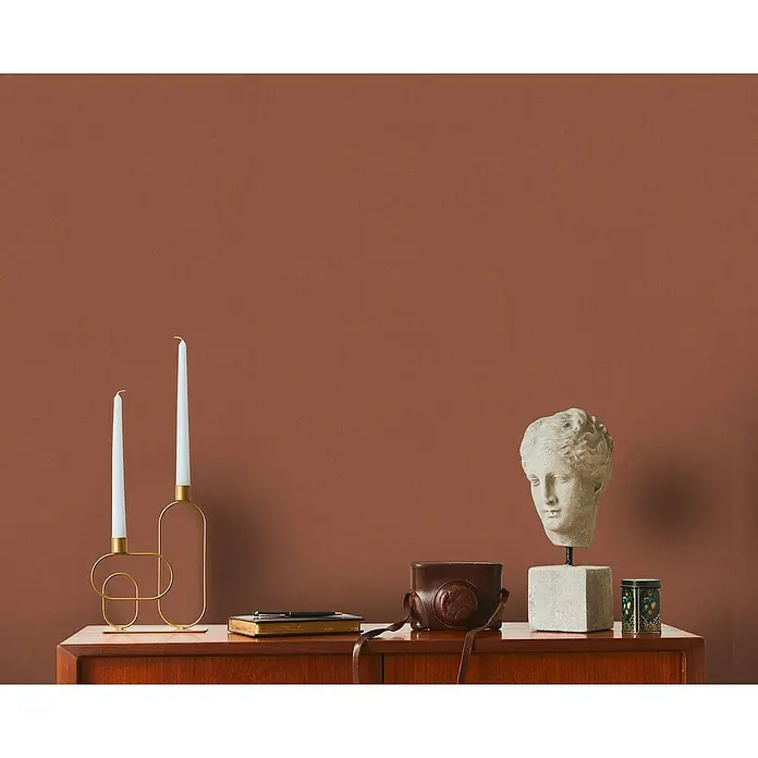 A.S. Création Metropolitan Stories Travel Styles Vliestapete - Rost, Uni, 10,05 x 0,53 m - Dekorative Anordnung mit Kerzenhaltern, Büste, Kamera und Dose auf einem Holzschrank vor einem einfarbigen Hintergrund.