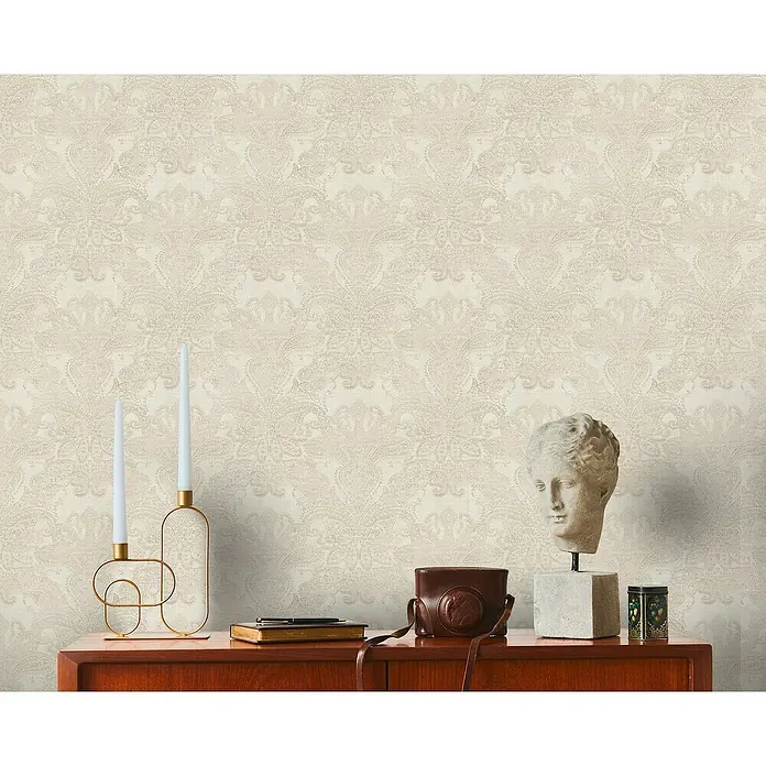 A.S. Création Metropolitan Stories Travel Styles Vliestapete DamaskCreme, Ornament, 10,05 x 0,53 m - Nahaufnahme eines Raumes mit einer Kommode, auf der eine Kopfskulptur, eine Kamera, Kerzen und ein Buch stehen.
