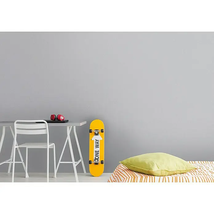 A.S. Création Metropolitan Stories Travel Styles Vliestapete - Melange-Hellgrau, Uni, 10,05 x 0,53 m - Das gelbe Skateboard mit dem Aufdruck "One Way" lehnt an einer grauen Wand, neben einem Tisch mit Kopfhörern.