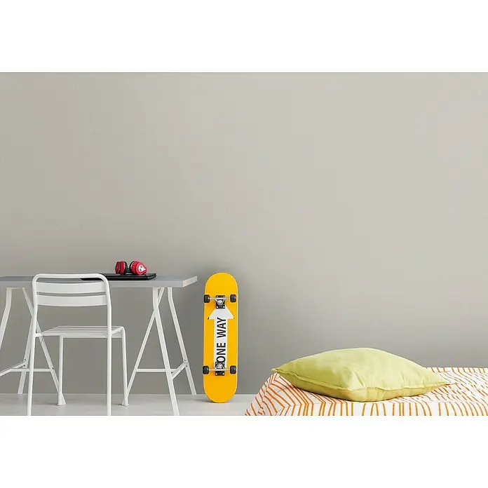 A.S. Création Metropolitan Stories Travel Styles Vliestapete - Melange-Beige, Uni, 10,05 x 0,53 m - Ein gelbes Skateboard mit der Aufschrift "One Way" lehnt an einer grauen Wand neben einem Schreibtisch mit Kopfhörern.
