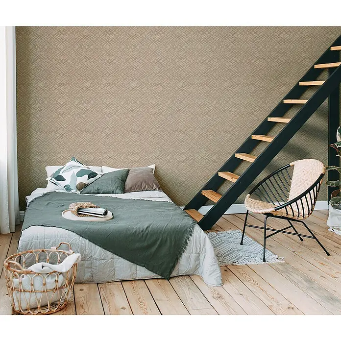 A.S. Création Metropolitan Stories Travel Styles Vliestapete Allover I - Beige/Gold, Grafisch, 10,05 x 0,53 m - Schlafzimmer mit großem Bett, Leiterregal und dekorativem Korbsessel auf hellem Holzboden vor einer gemusterten Tapete.
