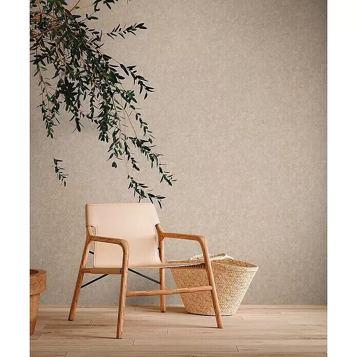 A.S. Création Metropolitan Stories Travel Styles Vliestapete - Dunkelbeige, Uni, 10,05 x 0,53 m, Feine Struktur - Moderner Stuhl mit hellem Holzrahmen und beigem Ledersitz, in einem Raum mit einem Korb und grünen Pflanzen.