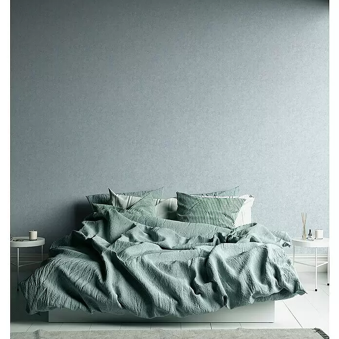 A.S. Création Metropolitan Stories Travel Styles Vliestapete - Hellblau, Uni, 10,05 x 0,53 m, Feine Struktur - Gemütliches Bett mit zerknitterter mintgrüner Leinenbettwäsche und gestreiften Kissen in einem Schlafzimmer mit blaugrauer Wand.