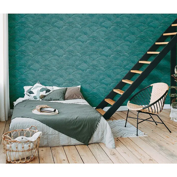 A.S. Création Metropolitan Stories Travel Styles Vliestapete - Grün, Wellen, 10,05 x 0,53 m - Gemütliches Schlafzimmer mit einem Bett, einem Rattansessel und einer Leiter, die zu einem erhöhten Bereich führt. Die grüne Wand verleiht dem Raum eine beruhigende Atmosphäre.