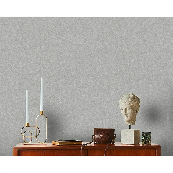 A.S. Création Metropolitan Stories Travel Styles Vliestapete - Melange-Grau, Uni, 10,05 x 0,53 m - Einrichtungsidee mit Kerzenständer, Skulptur und Kamera auf einer Kommode, die ein minimalistisches und künstlerisches Ambiente schaffen.