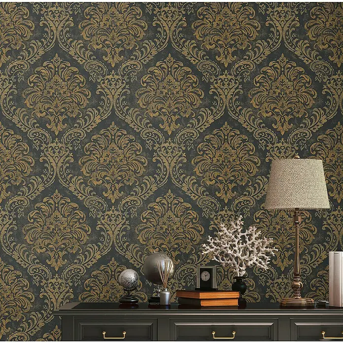 A.S. Création Metropolitan Stories Travel Styles Vliestapete Damask - Schwarz/Gold, Ornament, 10,05 x 0,53 m - Elegante Nahaufnahme eines schwarzen Schranks mit Dekorationsgegenständen vor einer Wand mit goldenem Damastmuster.