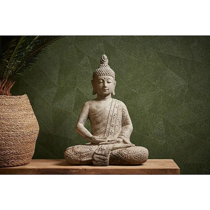 A.S. Création Metropolitan Stories Travel Styles Vliestapete - Grün, Grafisch, 10,05 x 0,53 m, Matt - Eine Buddha-Statue aus Stein sitzt friedlich auf einem Holztisch, neben einer Pflanze, vor einer grünen Wand mit geometrischem Muster.