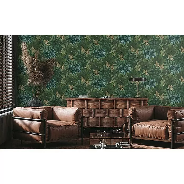 A.S. Création Metropolitan Stories Travel Styles Vliestapete - Grün/Gelb, Floral, 10,05 x 0,53 m - Tapete mit tropischen Blättern in Grün, Blau und Gold an einer Wohnzimmerwand hinter Ledersesseln.