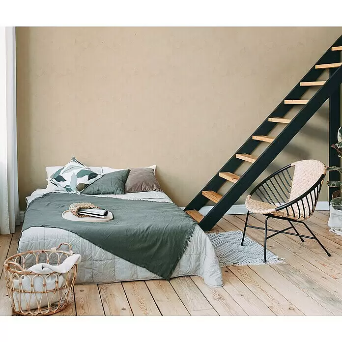 A.S. Création Metropolitan Stories Travel Styles Vliestapete - Beige, Grafisch, 10,05 x 0,53 m, Matt - Ein gemütliches Schlafzimmer mit einem Bett in olivgrüner und grauer Bettwäsche, einem Rattan-Stuhl und einer schwarzen Holztreppe.