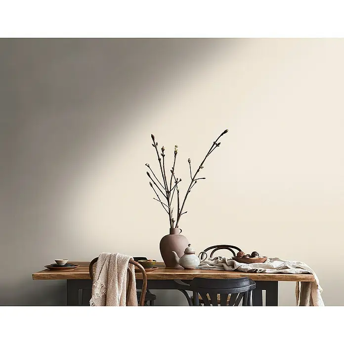 A.S. Création Metropolitan Stories Travel Styles Vliestapete - Melange-Creme, Uni, 10,05 x 0,53 m - Nahaufnahme eines Tisches mit Geschirr, einer Blumenvase und einem beigen Überwurf, der eine warme und einladende Atmosphäre schafft.