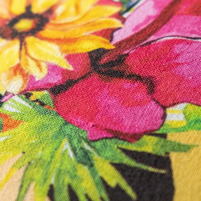 Kissen Kiki - Gelb, 45 x 45 cm, 100 % Baumwolle - Nahaufnahme eines bunten Stoffes mit Blumenmuster, der eine lebendige und detaillierte Textur zeigt, ideal für Mode oder Heimdekor.
