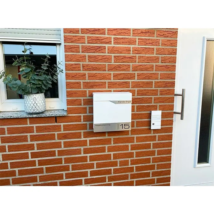 Metzler Wandbriefkasten Siebert - L x B x H: 10,5 x 37 x 37 cm, Verkehrsweiß, Stahl, Zeitungsfach - Fassadenansicht mit einem modernen Briefkasten mit Hausnummer 15 und dem Namen Familie Ergül, neben einer Haustür.