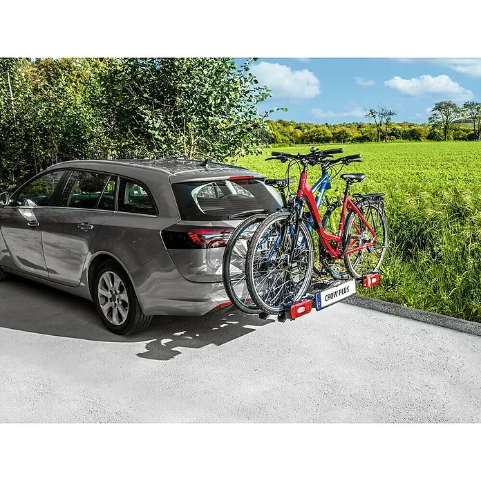 Eufab Portabicicletas Crow + - Apto para: 2 bicicletas, Capacidad de carga: 50 kg - Un coche familiar plateado transporta dos bicicletas en un portabicicletas CROW PLUS frente a un fondo rural.