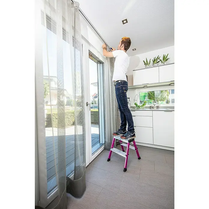 Krause Monto Klapptritt Rolly4 Stk., Arbeitshöhe: 2,45 m, Pink - Ein Mann steht auf einer pinkfarbenen Trittleiter und montiert eine Gardinenstange an der Decke.