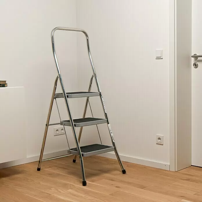 Krause Klapptritt Toppy XL - Anzahl Tritte: 3 Stk., Arbeitshöhe: 2,7 m, Belastbarkeit: 150 kg, Aluminium - Dreistufige silberne Stehleiter mit schwarzen Trittflächen steht bereit im Raum.