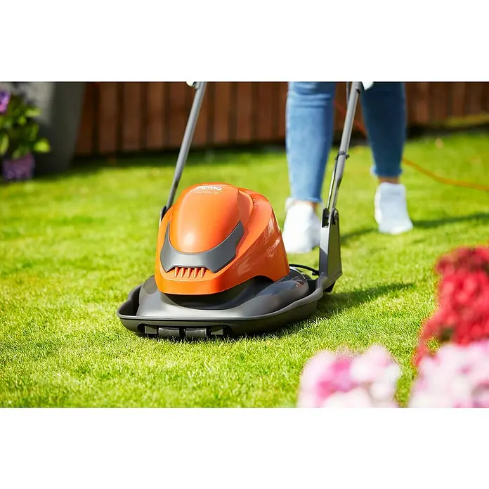 Flymo Elektro-Luftkissenmäher SimpliGlide 360 - Schnittbreite: 36 cm - Nahaufnahme eines orangefarbenen Flymo Rasenmähers auf einem grünen Rasen, der von einer Person bedient wird.