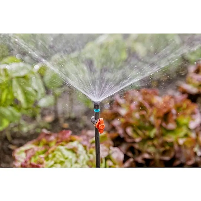 Gardena Micro-Drip Válvula de regulación - 3/16" x 4,6 mm, 4 ud. - Primer plano de un aspersor regando un macizo de flores con plantas verdes y rojas. El aspersor proporciona un riego eficiente.