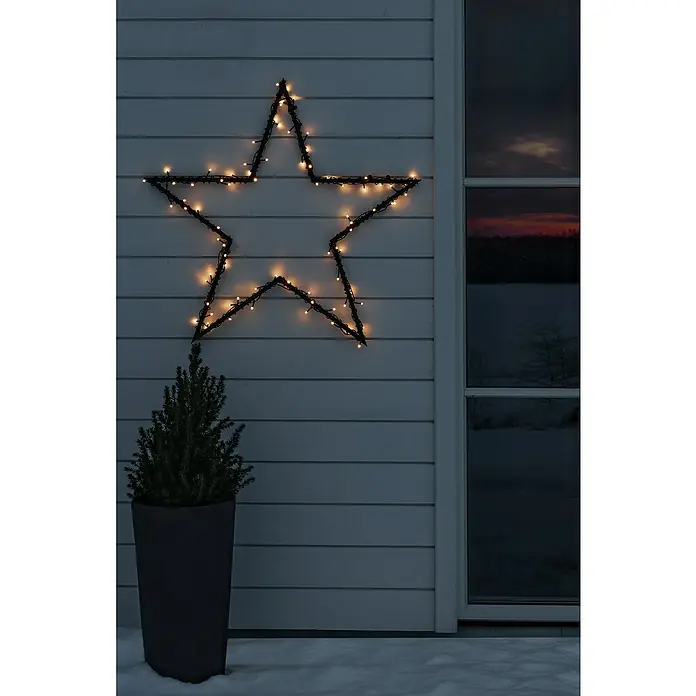 Konstsmide LED-LichterketteAußen, Lichtfarbe: Bernstein, Anzahl Leuchtmittel: 200 Stk., Solarbetrieben - Weihnachtsstern-Lichterkette schmückt die Wand neben einem Fenster und einer Topfpflanze im Schnee.