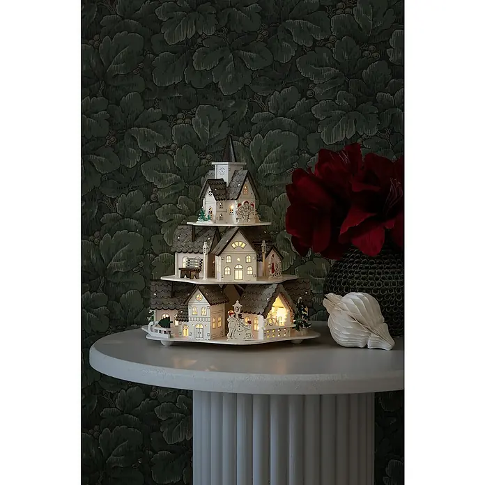 Konstsmide LED-Szenerie Häuser - L x B x H: 25,5 x 23 x 27,5 cm, Weiß, Batteriebetrieben, LED - Ein dreistöckiges Weihnachtsdorf mit beleuchteten Häusern auf einem Beistelltisch, eine festliche Dekoration.