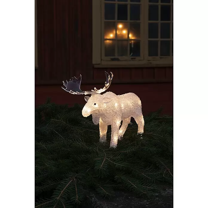 Konstsmide LED-Weihnachtsdekofigur LED Acryl - 32 x 26 x 10 cm, Farblos, Batteriebetrieben, LED, Elch - Beleuchtete weiße Elchdekoration auf Tannenzweigen, mit verschwommenem, festlichem Fenster im Hintergrund.