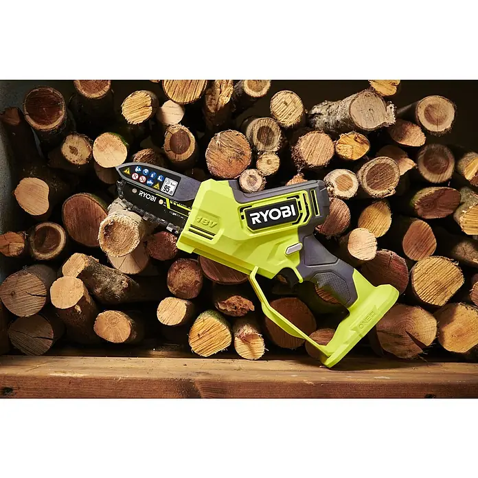 Ryobi ONE+ Akku-Astsäge RY18PSX10A-120 - 18 V, 2 Ah, Li-Ionen, 1 Akku, Schwertlänge: 10 cm - Nahaufnahme einer Ryobi Akku-Kettensäge vor einem Stapel Holzscheite, die die Kompaktheit und Effizienz des Werkzeugs hervorhebt.