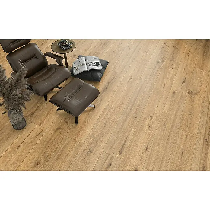 Classen Designboden Pro Nature - Soledad, Landhausdiele, 1.290 x 246 x 4 mm - Einladendes Wohnzimmer mit hellbraunem Laminatboden, einem Ledersessel und einem kleinen Beistelltisch mit Buch. Gemütliche Atmosphäre.