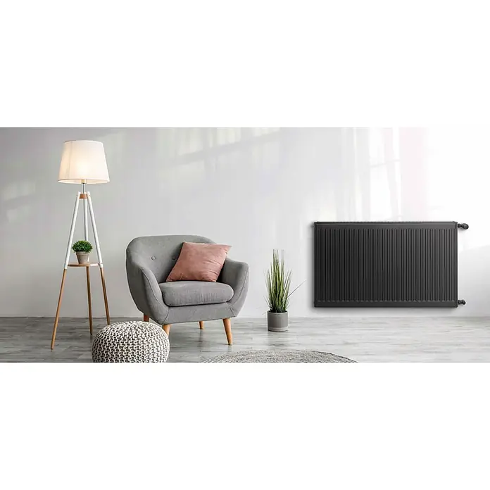 Sanicomfort Kompaktheizkörper - B x H: 1.000 x 600 mm, Wärmeleistung bei Vorlauftemperatur von 75 °C (D: 50): 1.653 W, Typ Heizkörper: 22 - Ein stilvolles Zimmer mit einem schwarzen Heizkörper an der Wand, einem Sessel, einer Stehlampe und dekorativen Pflanzen.