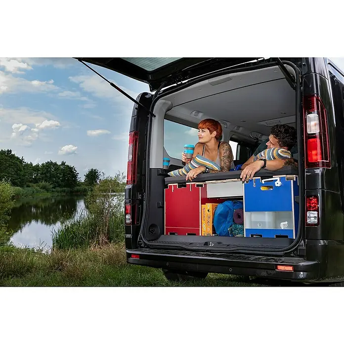 Vojo Camper Ausbau-Set City Break - 18 -tlg., Geeignet für: Transporter - Ein Paar entspannt im Heck eines schwarzen Vans, der mit Campingmöbeln ausgestattet ist, Blick auf einen ruhigen See.