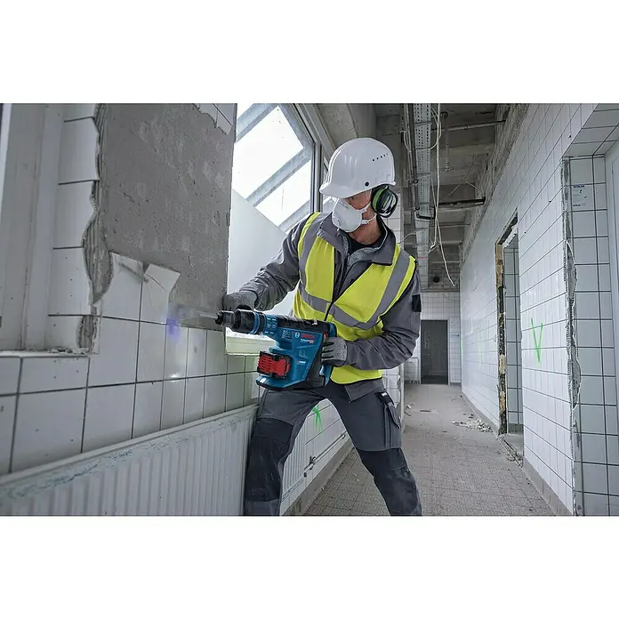 Bosch Professional AMPShare 18V Akku-Kombihammer GBH 18V-40 C18 V, Ohne Akku, 9 J - Ein Bauarbeiter mit Helm demoliert eine Wand mit einem Bosch Abbruchhammer. Der Hammer ist blau, rot und hat eine große Batterie.