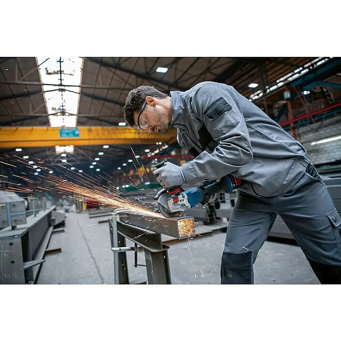 Bosch Professional AMPShare 18V Akku-Winkelschleifer GWS 18V-15 P - 18 V, Ohne Akku, Durchmesser Scheibe: 125 mm - Ein Mann in Arbeitskleidung benutzt einen Winkelschleifer, um ein Metallstück zu bearbeiten, wobei Funken sprühen. Schutzbrille und Handschuhe sind Teil der Sicherheitsausrüstung.