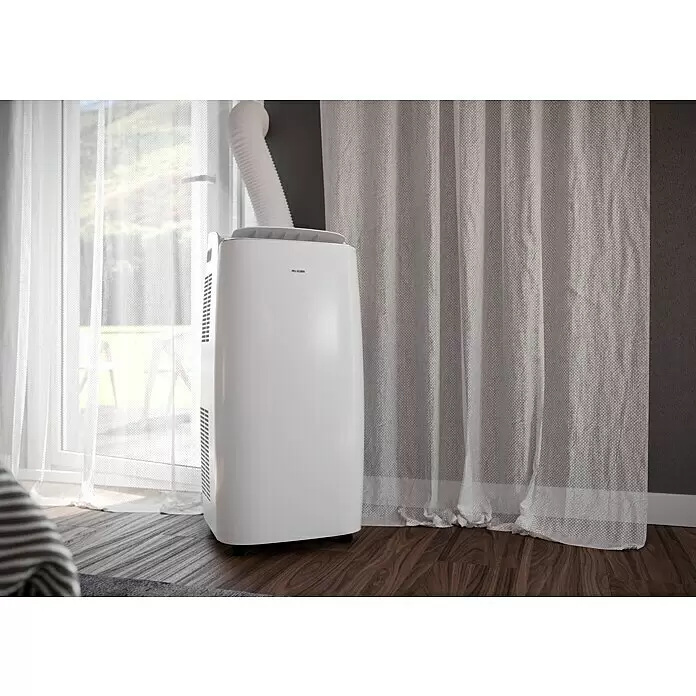 PR Klima Aire acondicionado portátil Moma - 3.500 W, Tamaño de la estancia: 35 m², Blanco - Aire acondicionado portátil blanco con manguera de escape, colocado junto a una ventana con cortinas sobre suelo de madera.