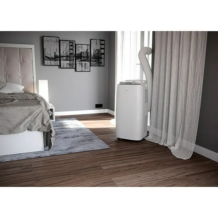 PR Klima Aire acondicionado portátil Moma - 3.500 W, Tamaño de la estancia: 35 m², Blanco - Un aire acondicionado portátil Olimpia Splendid se encuentra en un dormitorio amueblado de forma moderna cerca de una ventana con cortinas.