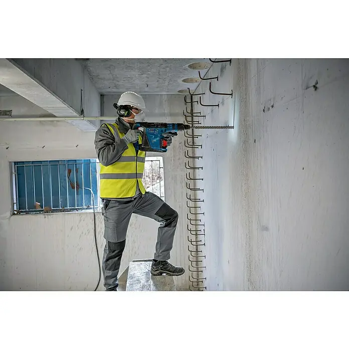 Bosch Professional AMPShare 18V Akku-Kombihammer GBH 18V-40 C - 18 V, 2 Akkus, 8 Ah, 9 J - Ein Bauarbeiter bohrt mit einem Bosch Bohrhammer in eine Betonwand, geschützt mit Helm und Maske.