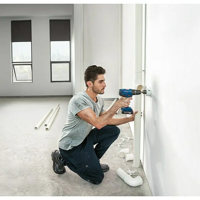 Bosch Professional AMPShare 18V Akku-Schlagbohrschrauber GSB 18V-21 - 18 V, 3 Akkus, 3 Ah - Ein Mann bohrt mit einem blauen Bosch Akku-Bohrschrauber ein Loch in eine Wand. Die Bohrmaschine ist kabellos und hat einen 18V Akku.