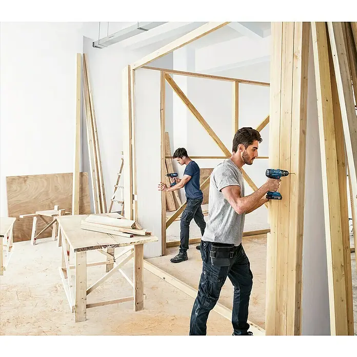 Bosch Professional AMPShare 18V Akku-Schlagbohrschrauber GSB 18V-21 - 18 V, 3 Akkus, 3 Ah - Zwei Handwerker arbeiten mit Bosch Akku-Bohrschraubern an einem Holzbauprojekt. Die blauen Bohrschrauber sind gut sichtbar und im Einsatz.