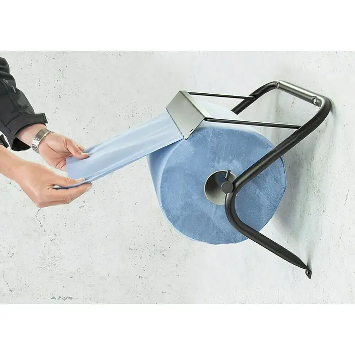Papierrollenhalter - 36,5 x 51 x 21,5 cm, Passend für: Putztuchrollen bis 40 cm Breite und max. 38 cm Durchmesser - Eine Person zieht ein blaues Papierhandtuch von einem schwarzen Rollenhalter mit einer silbernen Abrisskante.