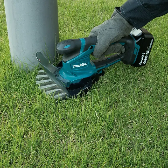 Makita LXT 18V Akku-Gras- & Strauchschere DUM604ZX - 18 V, Li-Ionen, Ohne Akku, Schwertbreite: 16 cm - Bild einer Makita Akku-Grasschere im Einsatz, die Gras um einen Pfosten herum schneidet.