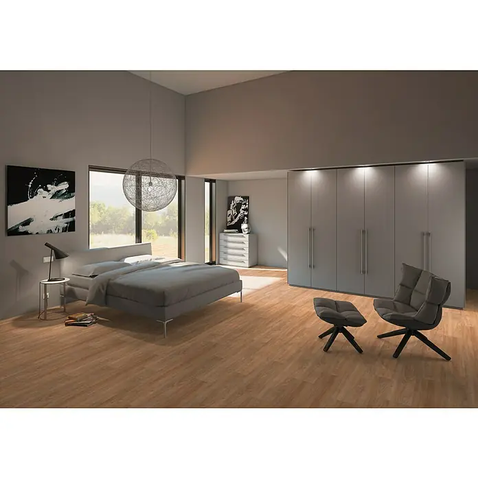 b!design Vinylboden Clic - Aspen Eiche, Landhausdiele, 1.210 x 190 x 5 mm - Schlafzimmer mit großem Schrank, Bett und Sessel. Das elegante Design schafft eine moderne und komfortable Atmosphäre zum Entspannen.