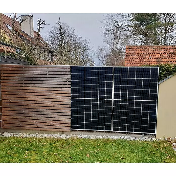 BRIGX Winkel - L x B x H: 596 x 40 x 20 mm, Passend für: Stabmatten - Zwei schwarze Solarpaneele in einem Holzzaun mit weißen Steinen und grünem Gras.