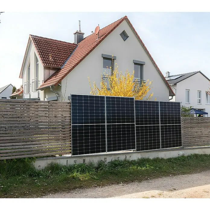 BRIGX Winkel - L x B x H: 596 x 40 x 20 mm, Passend für: Stabmatten - Diese Aufnahme zeigt eine Gruppe von Solarzellen, die an einem Zaun vor einem Haus angebracht sind. Die Paneele sind rechteckig und dunkel gefärbt.