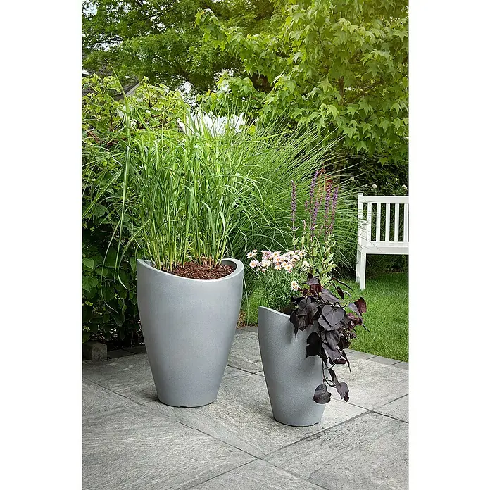 Scheurich Wave Globe Pflanzsäule rundAußenmaß (Ø x H): 49,6 x 67 cm, Kunststoff, Steingrau - Zwei graue Pflanzgefäße im Garten. Der größere Kübel ist mit Ziergras bepflanzt, während der kleinere Kübel mit verschiedenen Blumen und dunkelblättrigen Pflanzen bepflanzt ist.