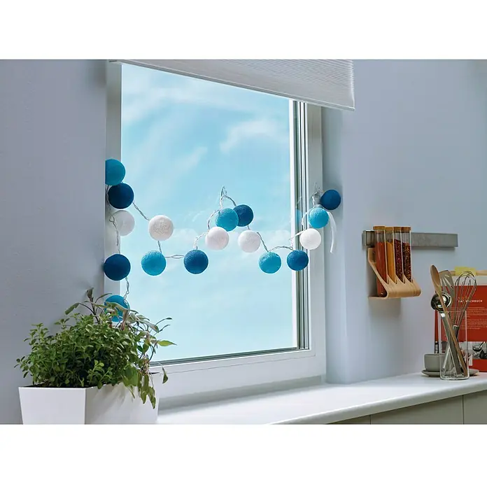Tesa Colgador adhesivo - Transparente, Carga soportada: 0,2 kg, 5 ud. - Guirnalda de luces de bolas de algodón azules y blancas colgando en una ventana con una planta en maceta en el alféizar, creando un ambiente acogedor.