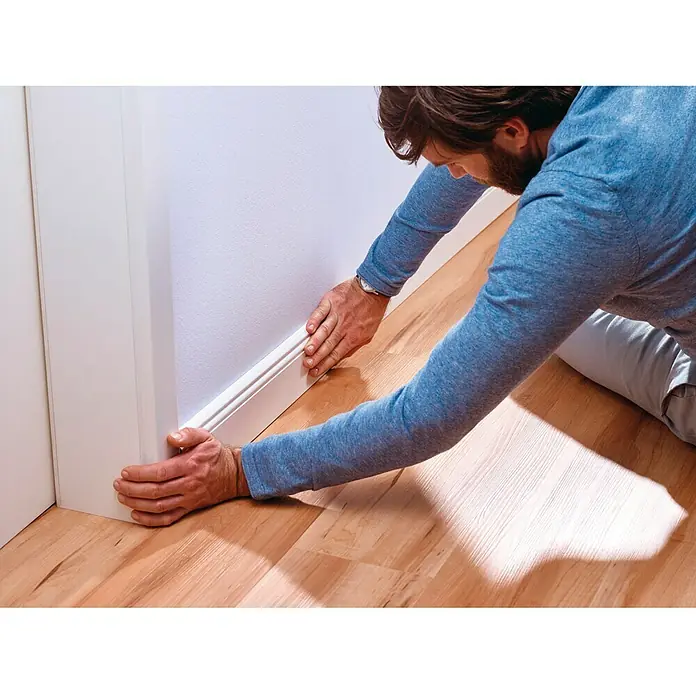 Tesa Powerbond Cinta de doble cara Paredes pintadas/Yeso - L x An: 5 m x 1,9 cm, Blanco - Un artesano instala zócalos blancos a lo largo de una pared para una transición limpia de piso a pared.