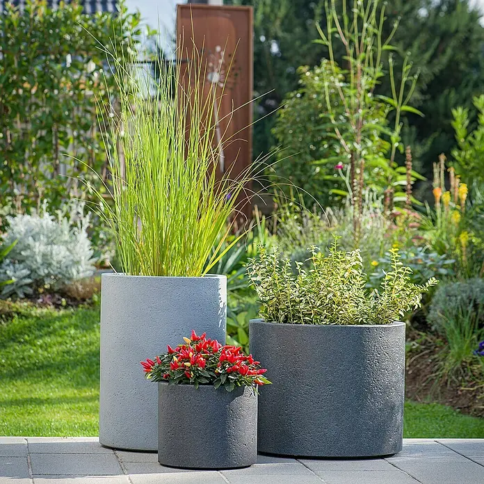 Scheurich Riva Pflanzsäule rund - Außenmaß (Ø x H): 38,5 x 53,4 cm, Kunststoff, Granitschwarz - Drei zylindrische Pflanzgefäße in verschiedenen Größen mit Pflanzen auf einer gepflasterten Fläche.