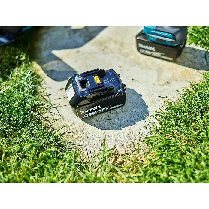 Makita LXT 18V Akku & Ladegerät Power Source Kit - 18 V, 2 Akkus, 5 Ah - Makita 18V 5.0Ah Akku, ideal für kabellose Elektrowerkzeuge, liegt auf einer Betonoberfläche mit Gras.
