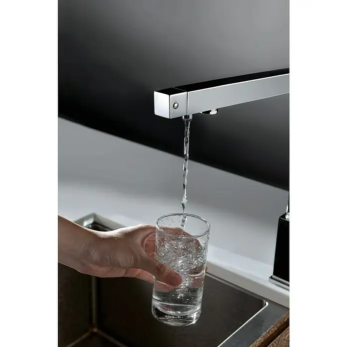 Imex Grifo de cocina ósmosis Capri - Cromo - Un moderno grifo cromado cuadrado llena un vaso con agua fresca sobre un elegante fondo minimalista.
