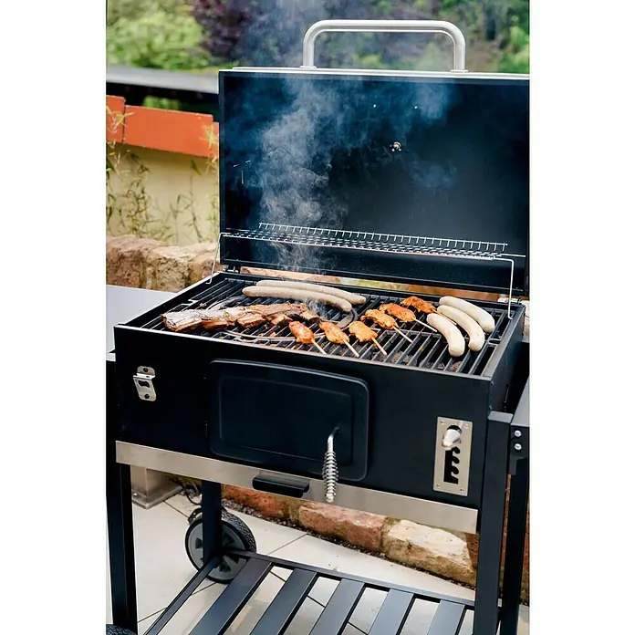 Kingstone KMS Holzkohlegrill Black Angus XXL - Grillfläche (B x T): 70 x 43,5 cm, Schwarz - Ein Holzkohlegrill mit einer Auswahl an Speisen, darunter Würstchen und Spieße, die auf dem Grillrost zubereitet werden.